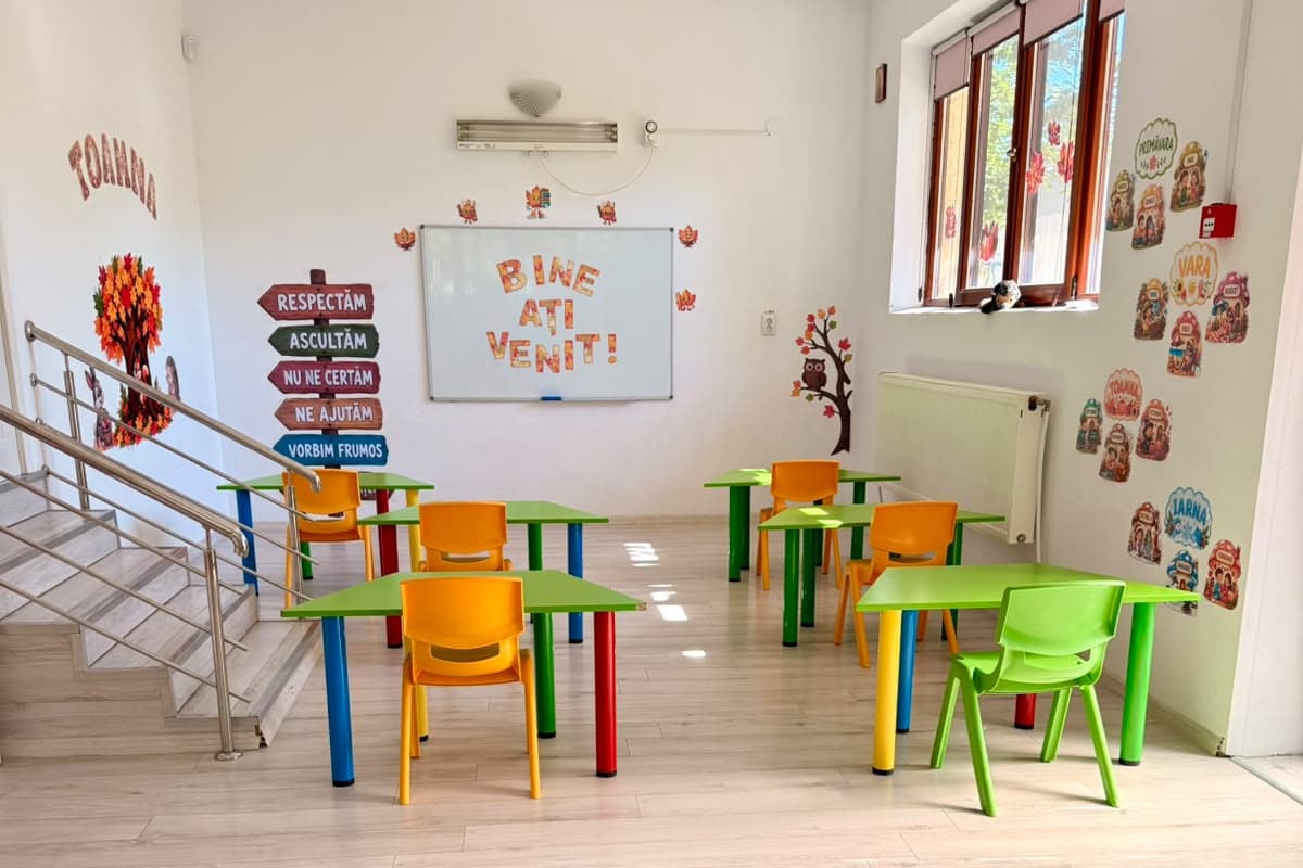 Sala de afterschool, cu scara spre etaj și mese pentru teme