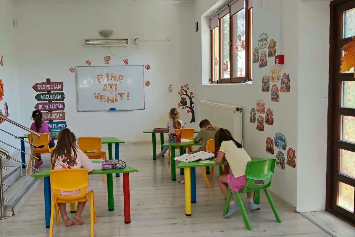 Copii la mese, făcând teme, lângă indicatorul cu regulile grupei
