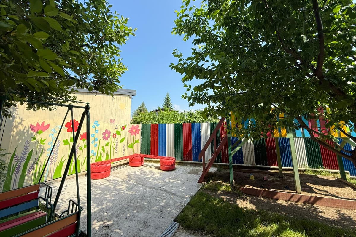 Perete pictat cu flori, cu bancă din anvelope colorate, lângă groapa de nisip