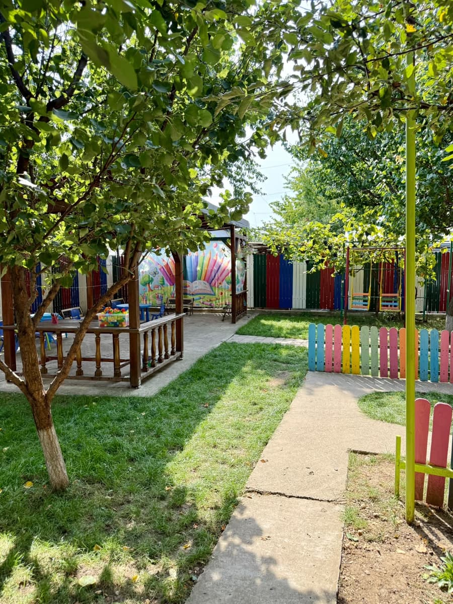 Gazebo cu mese de lucru, sub pomi, lângă peretele pictat cu un curcubeu de creioane