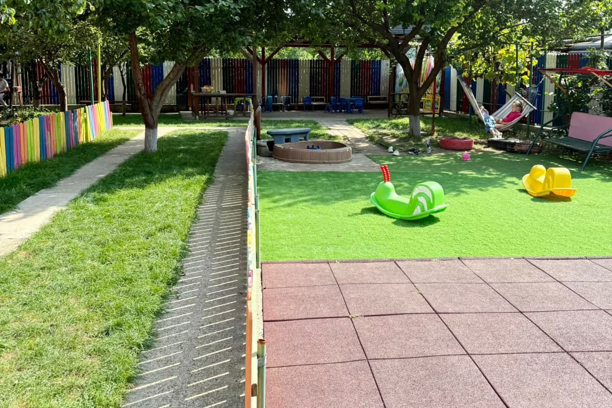 Gazonul sintetic cu balansoar verde și hamac, printre pomi