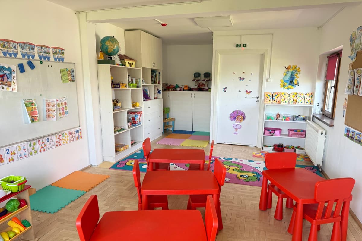 Sala mare, cu măsuțe roșii, glob și rafturi cu jucării și cărți